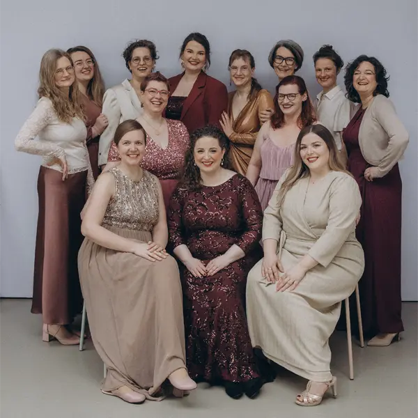 Gruppenfoto des Frauenkammerchors unmuted – zwölf Sängerinnen lächeln in festlicher, eleganter Kleidung im Studio.
